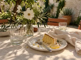 A slice of cake left on a linen table among flowers.
