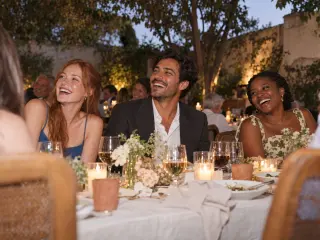 Guests laughing at a candlelit table at dusk.