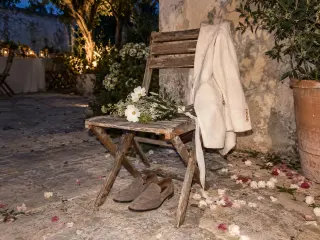 An empty chair with a jacket left on it, petals on the ground.